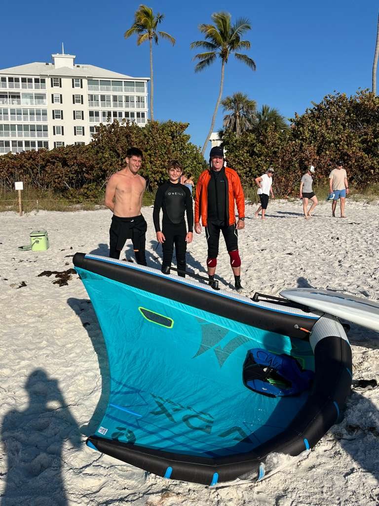 Will, Jack, and a friend standing on the beach with a wing laid out in front of them, ready to launch.