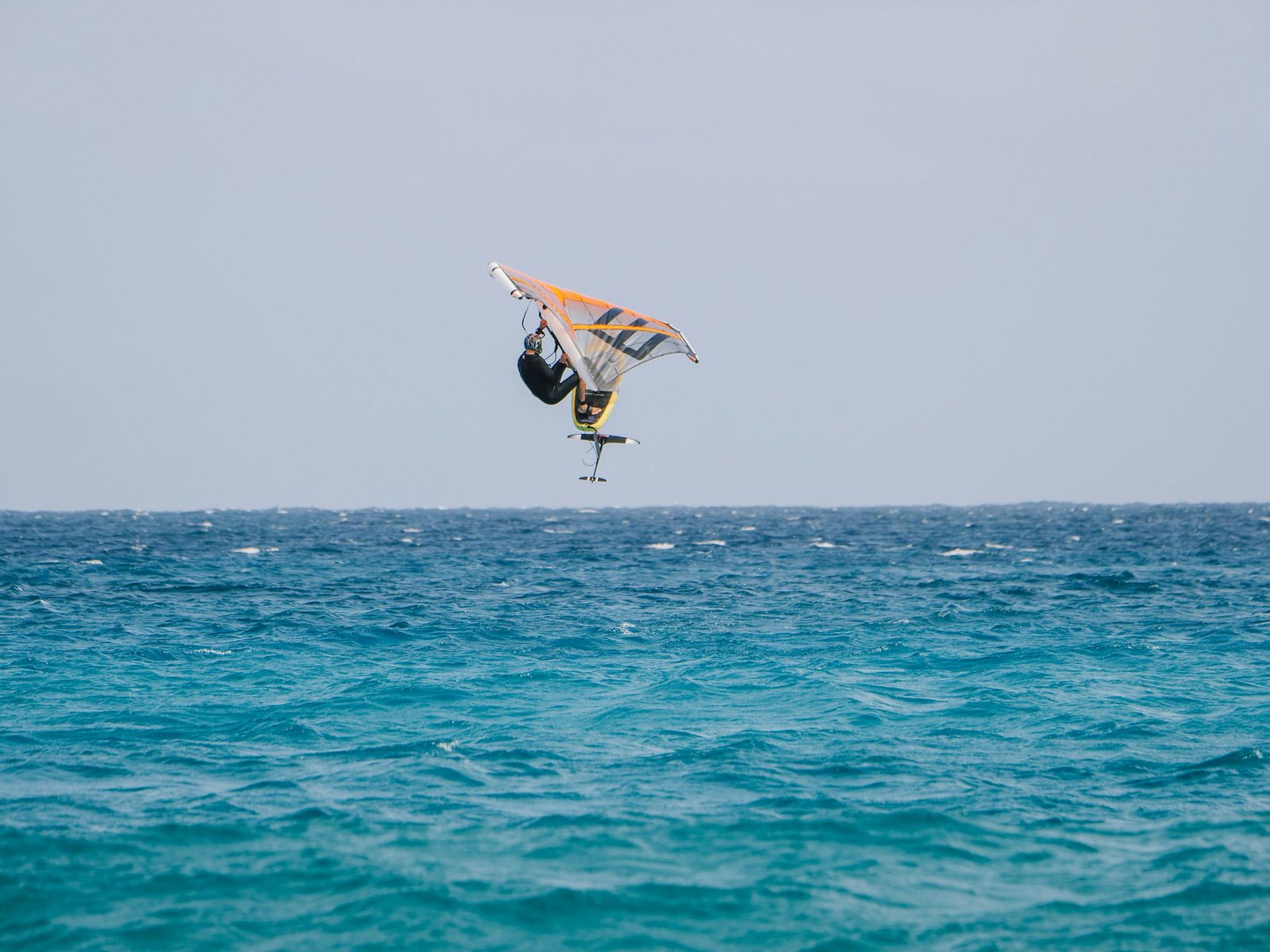 A wing foiler airborne, mid-jump above the water.