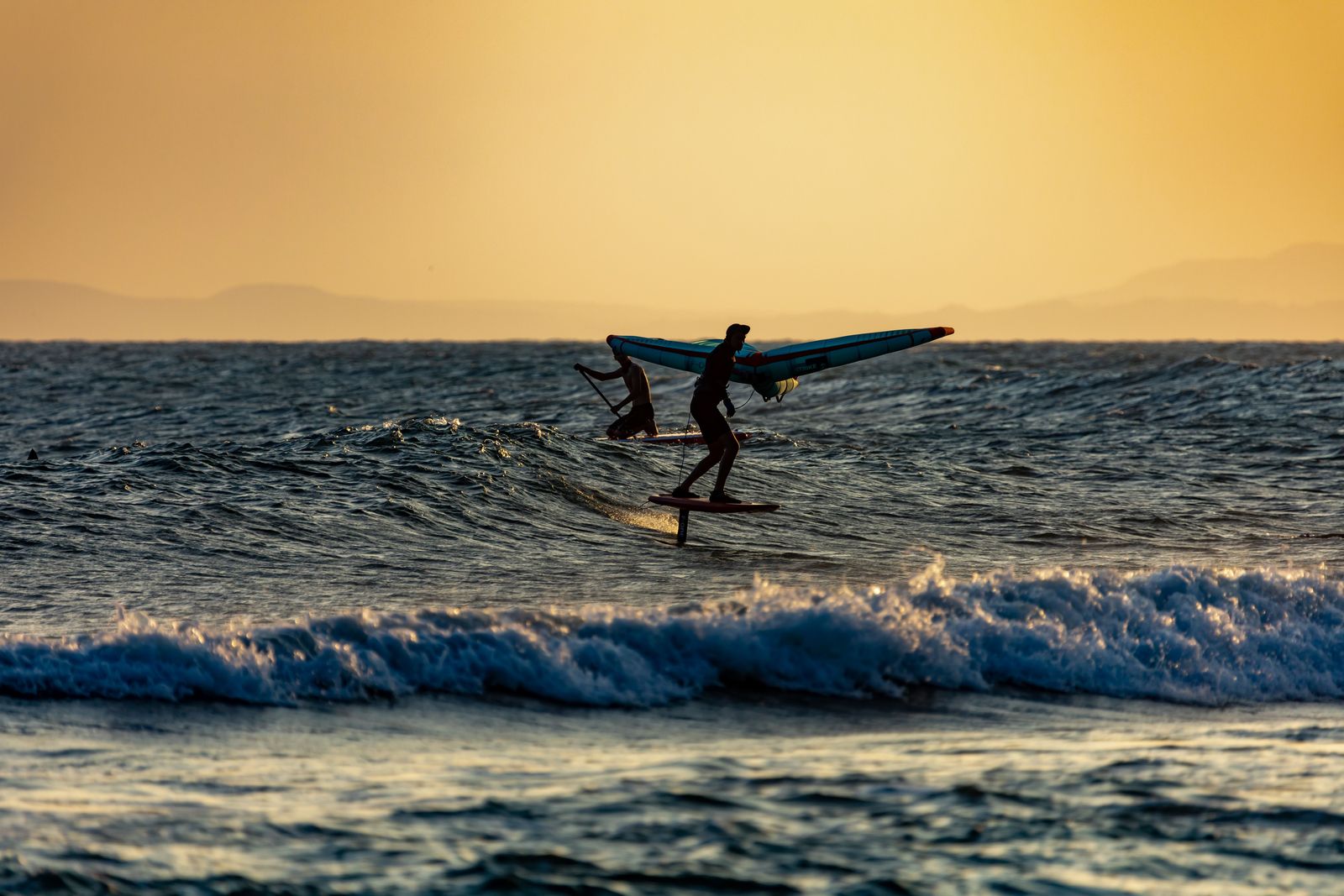 A wing foiler riding a wave at sunset.